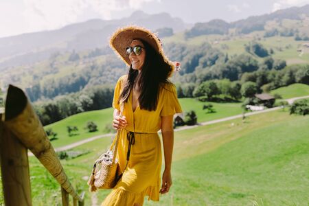 attractive woman in summer dress travel countryside and green meadow. Woman wearing sunglasses and hat relax in green countryside village. Switzerland. Active summer vacationの写真素材