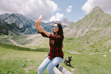 happy woman travel with dog and using smartphone in countrysideの写真素材