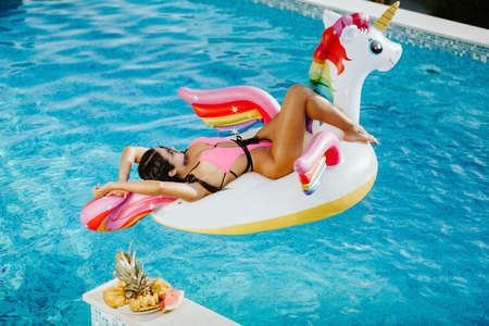sexy woman lay on inflatable beach floaty toy unicorn in swimming poolの写真素材