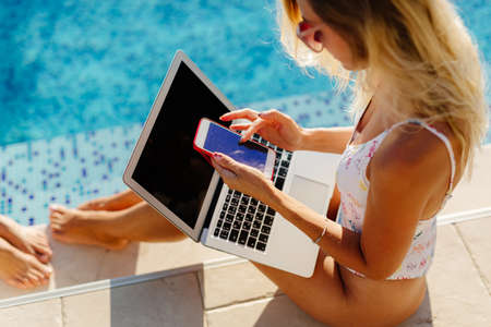 woman using laptop and smartphone on beach poolの写真素材