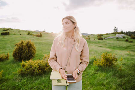 smiling girl using smartphone at countryside green meadow at sunsetの写真素材
