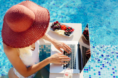 woman using laptop and work remotely near swimming poolの写真素材
