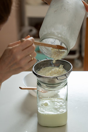Vertical shot showing a persons hands holding a glass jar to pour fermented milk and kefir grains...