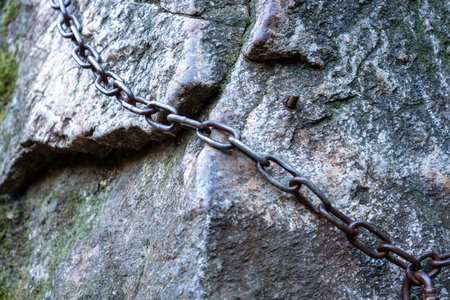 Close-up of a heavy metal chain anchored to a rock face for hikers.の写真素材