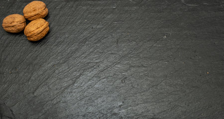 Top view of three whole walnuts in shell arranged on a dark black slate plate with ample copy space....