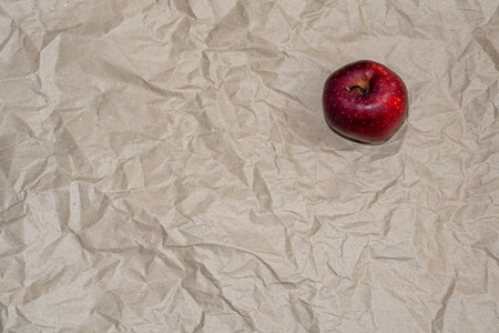 Red apple centered on wrinkled paper background with diffused natural light.