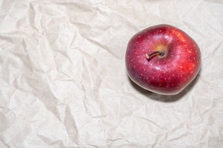 Top view of a ripe red apple centered on a textured kraft paper surface.の写真素材