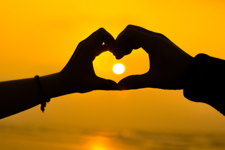 couple hands making a heart love sign sillhoute during sunrise at a beachの写真素材