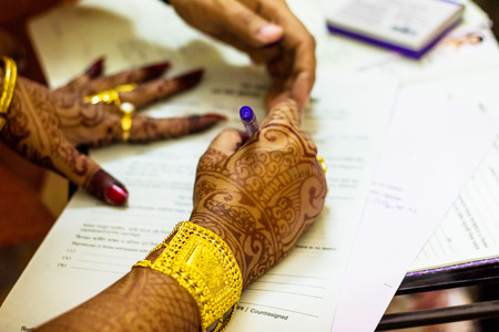 a newly married indian bengali wife with golden ornament and blacelet signing marriage registration formの写真素材