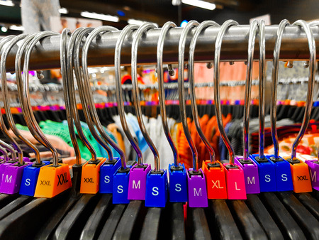 Different sized hanger with colourful dress size tags XL L M XS t shirts displayed in shop for sale