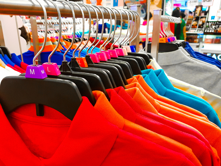 Different sized hanger with colourful dress size tags XL L M XS t shirts displayed in shop for sale