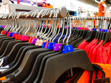 Different sized hanger with colourful dress size tags XL L M XS t shirts displayed in shop for saleの写真素材