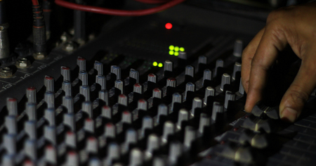 hands operating knobs of light and sound board console at a concert theater