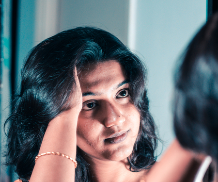 a lady handling and styling her hair by looking at mirror imageの写真素材