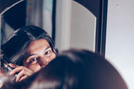 lady combing her hair with hairbrush at mirror.の写真素材