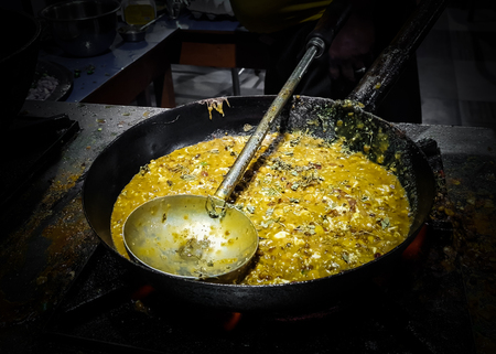 a chef cooking tadka fry in a frying pan at a road side food corner on a stove over flames