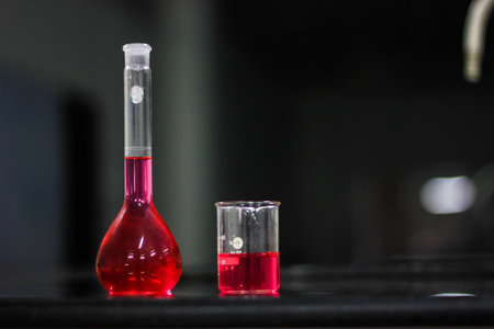 red liquid in a round bottomed flask and glass beaker on a black granite table in dark backgroundの写真素材