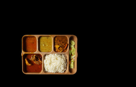 indian chicken thali with rice dal chicken salad vegetable curry on a plastic segmented plate in black backgroundの写真素材
