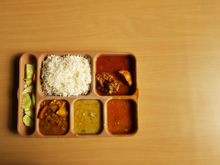indian chicken thali with rice dal chicken salad vegetable curry on a plastic segmented plate in wooden backgroundの写真素材