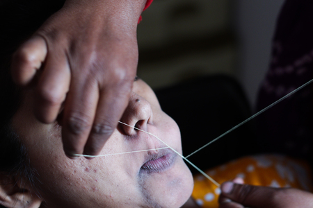 painful plucking and removal of upper lip hairs of a lady with threading. epilation cosmetic procedure in beauty parlour.の写真素材