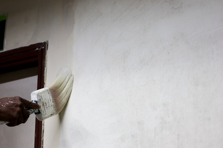 painting white paint on a wall with a paint brushの写真素材