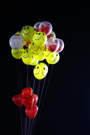 smile emoji shaped yellow balloon and heart shaped red balloons tied in bunch with threads in black backgroundの写真素材