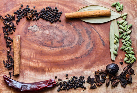 Typical ingredients for a garam masala black peppercorns, mace, cinnamon, cloves, dried red chilli and green cardamom in a wooden backgroundの写真素材