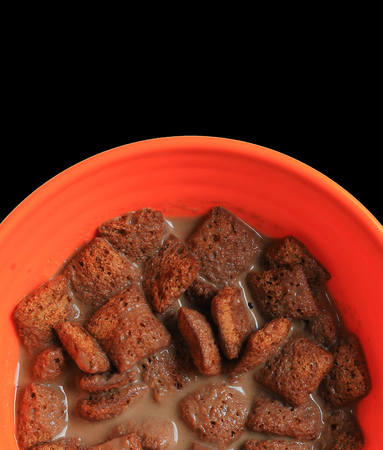 close up photo of chocolate cornflakes dipped in chocolate milk in black background