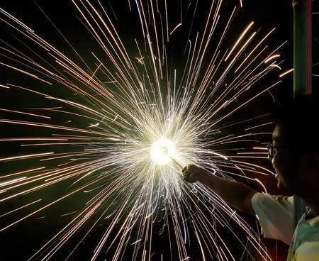 a man holding hand charki, a hand firework emitting circular sparks in black backgroundの写真素材