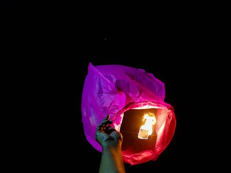 sky lantern lighting by a pair of hands holding the paper hot air balloon in a black backgroundの写真素材