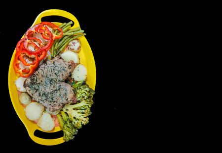 plate of steak and vegetables on a yellow plate on a black background with space for textの写真素材