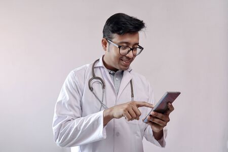 male indian doctor in white coat and stethoscope touching smart phoneの写真素材