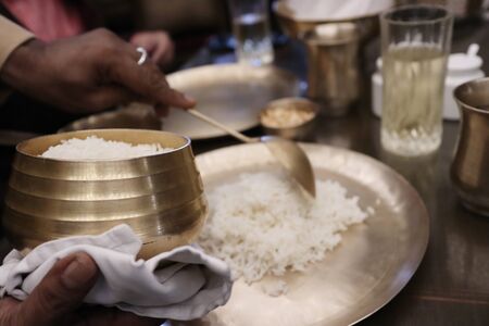 White boiled rice being served at a hotel on a brass bowl by a ladel on a brass plate