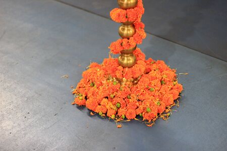marigold flowers chain wrapped around brass lamp stand base.