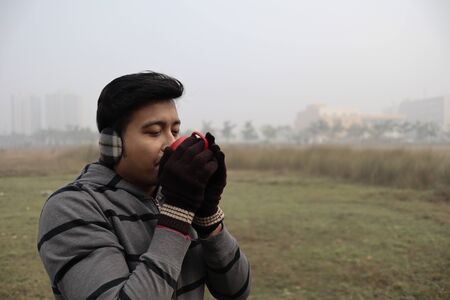 a man drinking hot coffee from a red cup and dressed in winter garments and gloves with focus on...