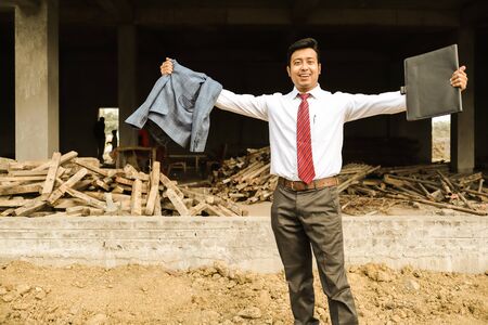 an young engineer in formal suit and pant with portfolio near a construction site feeling confident and celebrating joy with both hands in air.の写真素材