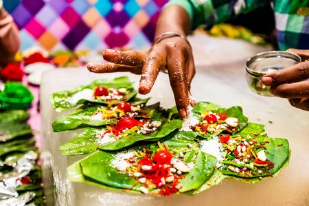 a hand sprinkling pan masala garnish and cherry on betel leaf during preparation of banarasi pan.の写真素材