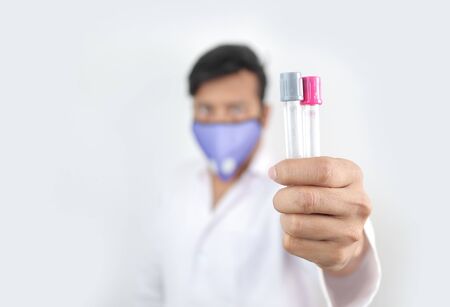 a medical professional in white coat and protective mask holding vials in hand with selective focus...