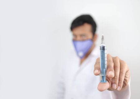 a medical professional in white coat and protective mask holding syringe in hand with selective focus in hand with blurred backgroundの写真素材
