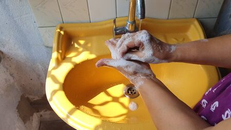 washing of both hands with soap under a yellow wash basin with running tap water to produce foam and...