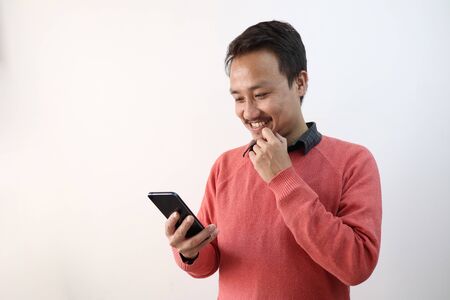 a man looking at his phone in a happy mood isolated in white background with space for textの写真素材