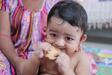 a newborn male toddler trying to bite a biscuit for the first time with his gumsの写真素材