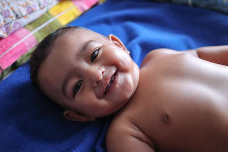 an infant toddler baby boy smiling on a blue towel looking at the camera in a happy moodの写真素材