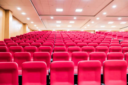 empty seats of an auditorium with red reclining rows of seats and false ceiling led lightsの写真素材