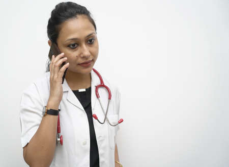 Hands of a doctor checking mobile phone in white coat and red stethoscope in white background.の写真素材