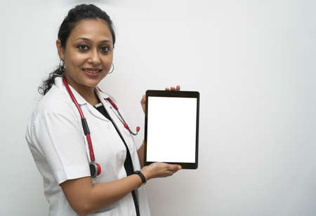 A south Indian female doctor in 30s holding tablet in white coat and red stethoscope in white background.の写真素材