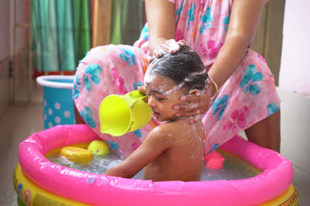 indian baby boy enjoying bath in an inflatable pool with water splashing and float toys.