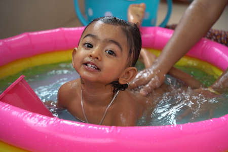 indian baby boy enjoying bath in an inflatable pool with water splashing and float toys.