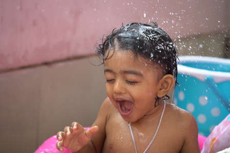 indian baby boy enjoying bath in an inflatable pool with water splashing and float toys.