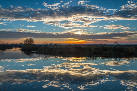 Sunrise over the lake with the reflection of bare trees in the waterの写真素材